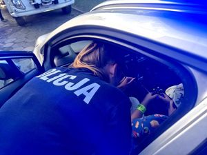 Na zdjęciu policjantka pochylająca się nad dzieckiem siedzącym w policyjnym radiowozie.