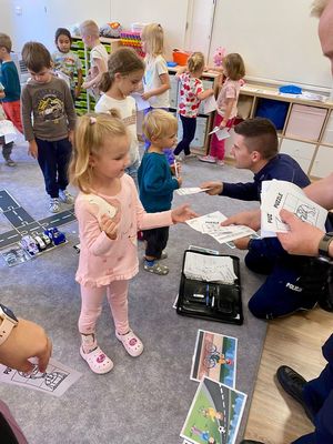 Na zdjęciu policjant rozdający dzieciom kolorowanki.