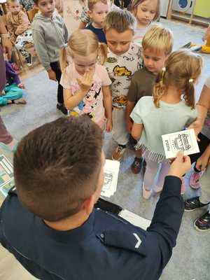 Na zdjęciu policjant wraz z przedszkolakami rozdający kolorowanki.