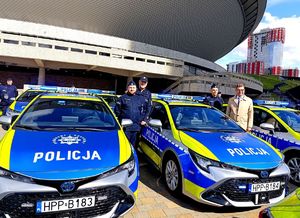 Na zdjęciu umundurowani policjanci stojący przy dwóch radiowozach służbowych.