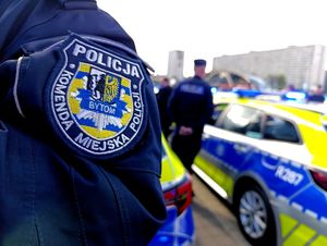 Na zdjęciu ramię policjanta, na nim emblemat z napisem Policja Komenda Miejska Policji Bytom, w tle radiowóz policyjny i policjanci.