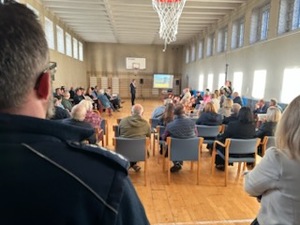 Na zdjęciu policjant stojący tyłem i zgromadzone osoby.