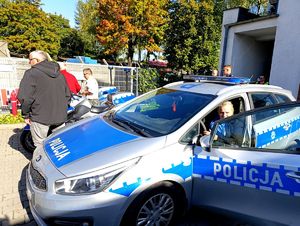 Na zdjęciu policjant siedząca w radiowozie kobieta, dookoła policjanci i uczestnicy wydarzenia.