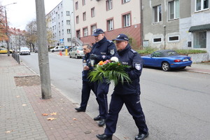 policjanci idący przez ulicę z kwiatami i zniczem