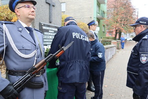 warta honorowa oraz komendant zapalający znicz przy tablicy upamiętniającej zmarłego policjanta