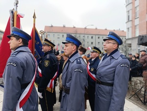 Na zdjęciu widzimy trzech policjantów stojących jeden za drugim, pierwszy z nich trzyma sztandar.