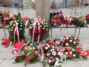 Na zdjęciu biało-czerwone wieńce i wiązanki ułożone pod pomnikiem,