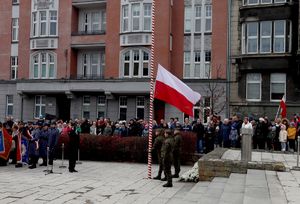 Na zdjęciu zgromadzone osoby oraz mundurowi wciągający biało czerwoną flagę na maszt.