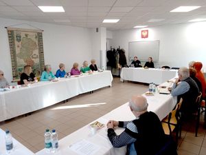 Na zdjęciu policjantka, policjant i seniorzy siedzący przy stołach.