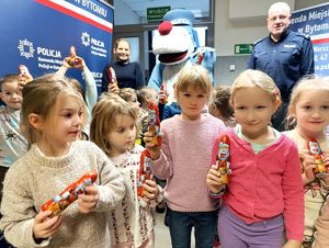 Na zdjęciu dzieci trzymające w dłoniach czekoladowe Mikołaje, policjantka, policjant i Sznupek.