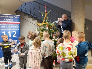 Na zdjęciu policjant ozdabiający z dziećmi choinkę