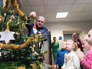 Na zdjęciu policjant ozdabiający z dziećmi choinkę