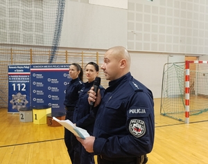 na zdjęciu policjant przemawiający do mikrofonu przy nim dwie policjantki