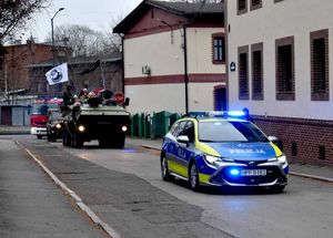 na zdjęciu jadący radiowóz, zanim wozy militarne w których znajdują się osoby ubrane w mikołajowe czapki, za nimi wóz strażacki