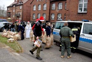 na zdjęciu osoby w mikołajowych kostiumach, strażacy i policjanci przenoszący worki i kartonowe pudełka do radiowozu