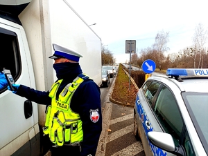 Policjant stojący prowadzący badania trzeźwości nadjeżdżających kierujących.