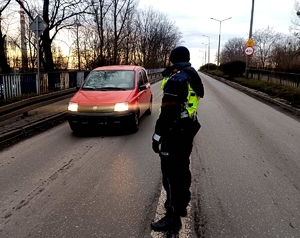 Policjant stojący na jezdni i prowadzący badania trzeźwości nadjeżdżających kierujących.