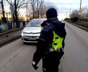 Policjant stojący na jezdni i prowadzący badania trzeźwości nadjeżdżających kierujących.