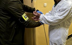 na zdjęciu policjant zakładający kajdanki zatrzymanemu mężczyźnie