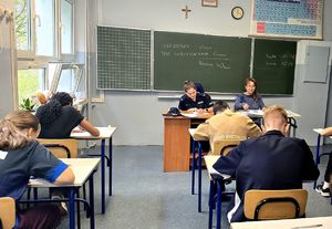 na zdjęciu uczniowie siedzący w ławkach przed nimi kobieta i policjantka