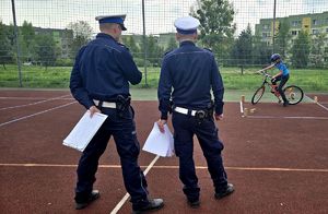 na zdjęciu znajdujący się na boisku 2 policjanci ruchu drogowego przed nimi chłopiec jadący na rowerze