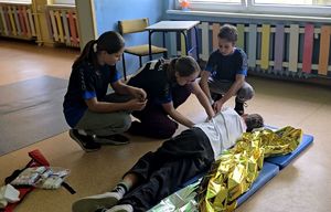 na zdjęciu chłopiec leżący na materacu przy nim trójka dzieci udzielająca mu pomocy