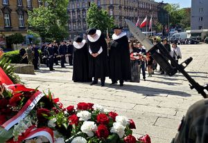 na zdjęciu osoby składające kwiaty przed pomnikiem