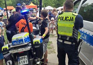 na zdjęciu policjant obok radiowóz służbowy oraz motocykl policyjny na którym siedzi dziecko