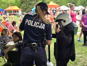na zdjęciu policjantka przy dziewczynce ubranej w policyjny kask, kamizelkę trzymająca w dłoni pałkę służbową