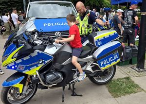 na zdjęciu policjant obok radiowóz służbowy oraz motocykl policyjny na którym siedzi dziecko