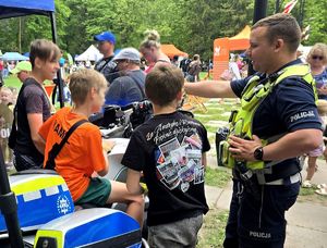 na zdjęciu policjant obok radiowóz służbowy oraz motocykl policyjny na którym siedzi dziecko