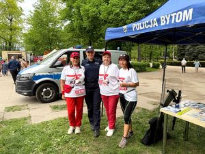 na zdjęciu policjantka i trzy kobiety ustawione przy niej i pozujące do zdjęcia, przy stoisku policyjnym, za nimi radiowóz służbowy oraz zgromadzone osoby