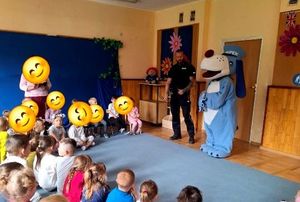 na zdjęciu policjant, sznupek i przedszkolaki siedzący na dywanie