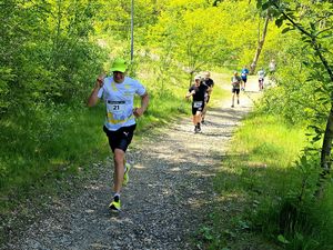 na zdjęciu mężczyzna z uniesionymi do góry palami w trakcie biegu, za nim kolejne biegnące osoby