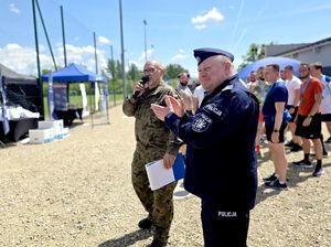 na zdjęciu komendant bijący brawa, za mim zgromadzone osoby i mundurowy trzymający mikrofon w dłoni