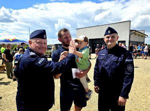 na zdjęciu komendant przybija piątkę z kilkuletnim chłopcem trzymanym na rękach mężczyzny obok kolejny policjant