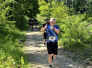 na zdjęciu mężczyzna z uniesionymi do góry kciukami w trakcie biegu, za nim kolejne biegnące osoby