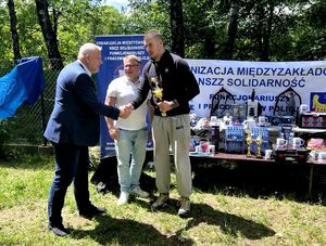 na zdjęciu zastępca komendanta podaje dłoń uczestnikowi zawodów, który trzyma puchar, obok przewodniczący związków