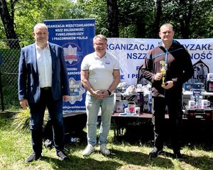 na zdjęciu zastępca komendanta,  obok przewodniczący związków i uczestnik zawodów, który trzyma puchar.