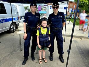 na zdjęciu dwie policjantki, pomiędzy nimi mały chłopiec ubrany w kask i kamizelkę policyjną