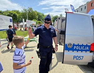na zdjęciu chłopiec i policjant przybijają sobie piątkę, stoją obok radiowozu policyjnego