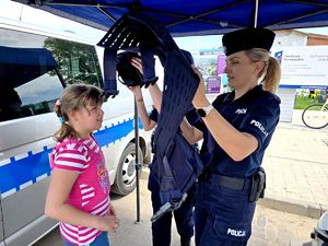 na zdjęciu dziewczynka, obok niej policjantka, która zakłada jej kamizelkę policyjną