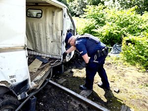 na zdjęciu policjant pochyla się i sprawdza wnętrze białego busa