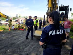 na zdjęciu policjantka odwrócona plecami, rozmyte tło na którym widoczni są kolejni mundurowi.