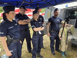 na zdjęciu dwie policjantki i trzej policjanci, przy nich chłopiec w stroju moro trzyma tarczę i pałkę policyjną