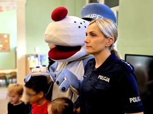 na zdjęciu policjantka, niebieska maskotka pies Sznupek i dzieci.