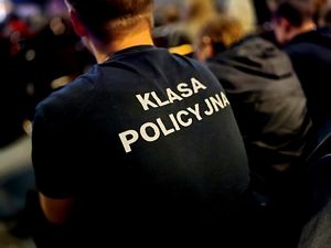 mężczyzna odwrócony plecami , na jego na czarnej koszulce biały napis klasa policyjna