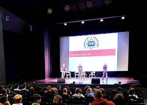 na scenie dwie policjantki i nieumundurowany policjant, za nimi wyświetlony  napis Policja Bytom Cyberbezpieczeństwo, przed nimi osoby siedzące na krzesłach w sali