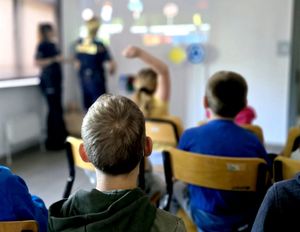 na zdjęciu dzieci siedzące na krzesłach, przed nimi dwie policjantki