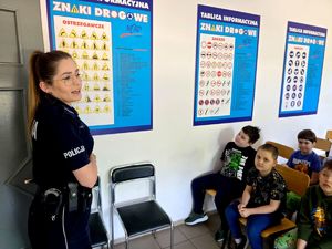 na zdjęciu policjantka , obok tablice przedstawiające znaki drogowe, obok dzieci na krzesłach w sali